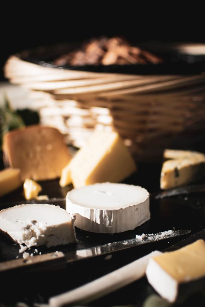 Close-up of various cheeses on a board with a blurred background basket.