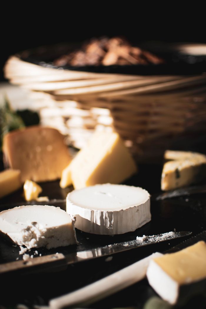 Close-up of various cheeses on a board with a blurred background basket.